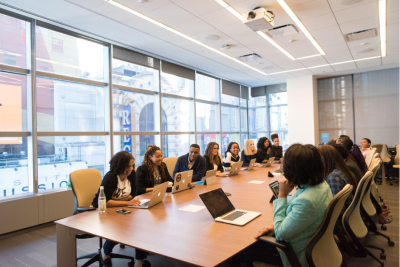 Diverse group of professionals engaged in a collaborative meeting around a large conference table in a bright, modern office space, emphasizing inclusivity and teamwork.