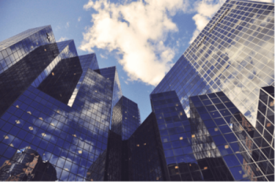 Modern skyscrapers with reflective glass facades under a partly cloudy sky, symbolizing the corporate landscape and oligopolies in Canada’s economy.