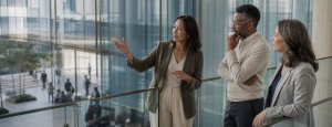 Three professionals, including Muraly Srinarayanathas, engaged in discussion near a large window, representing global leadership